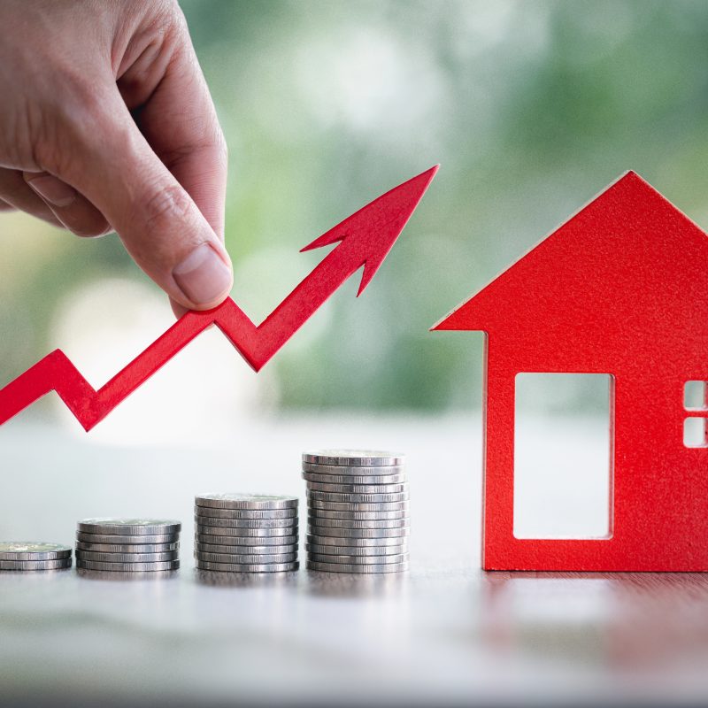 Stapels munten en een rood huis die de waardestijging van een woning symboliseren dankzij regelmatig onderhoud en renovatie