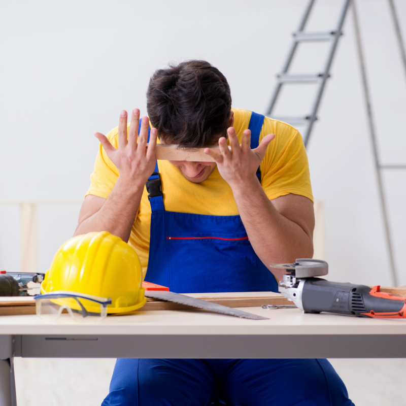 Worker in overalls sits at a workbench with tools, holding his head in frustration during a project.