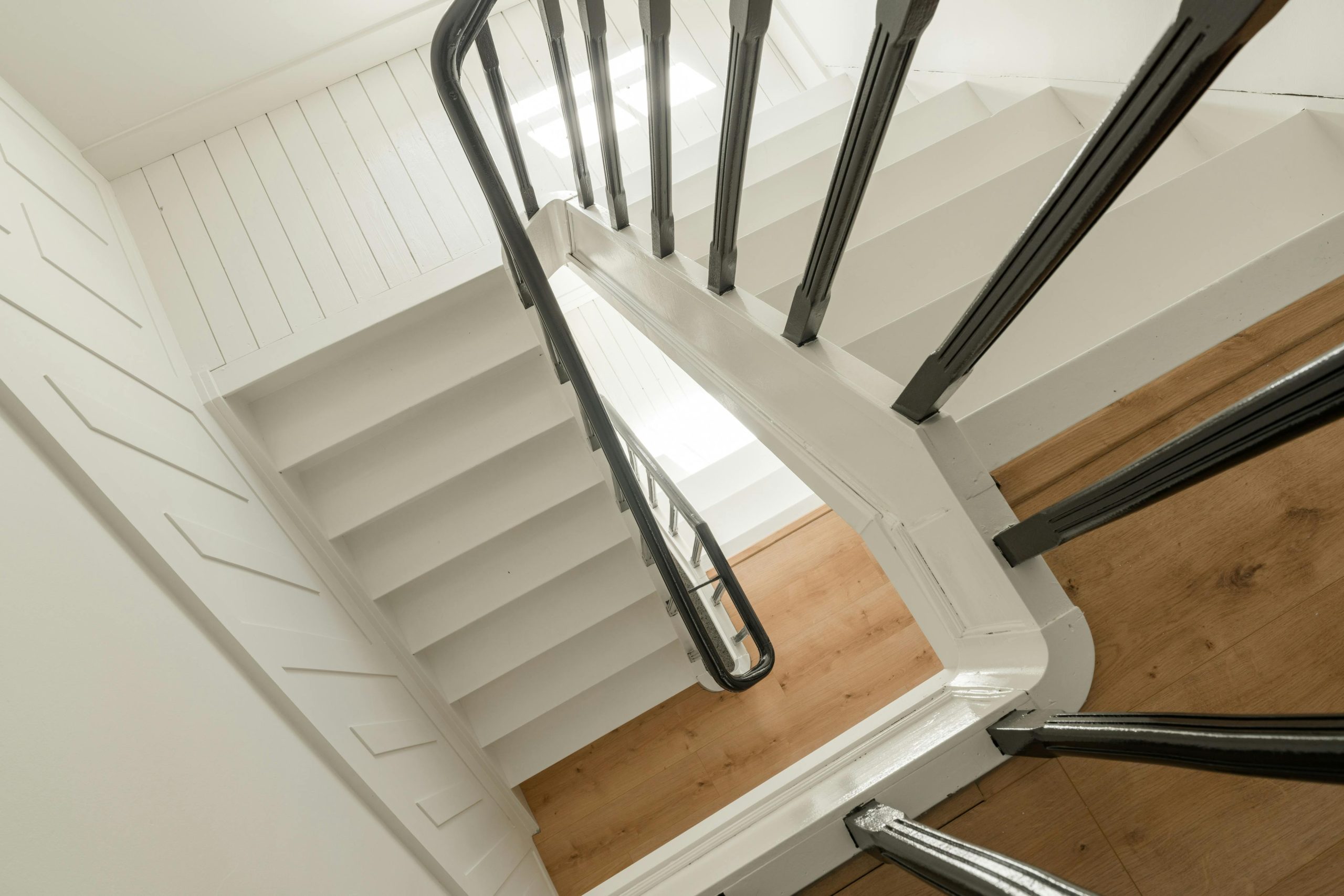 Een moderne, gerenoveerde trap met witte treden en donkere leuningen, gezien van bovenaf in een licht interieur.