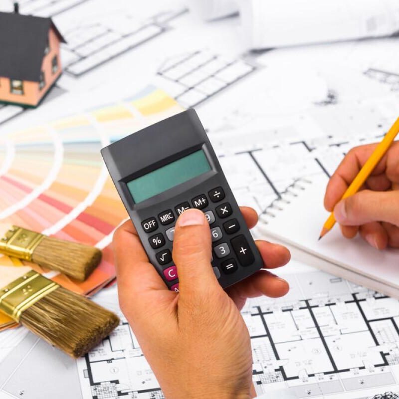 Een calculator, bouwtekeningen, verfstalen en kwasten op tafel symboliseren een slimme renovatieplanning en een zorgvuldig beheerd budget voor een woningrenovatie.