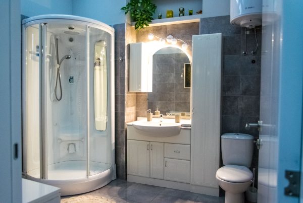 Deze moderne badkamer combineert een praktische indeling met lichte meubels en grijze tegels. De ruime douchecabine en sfeervolle verlichting zorgen voor comfort en een rustige uitstraling.