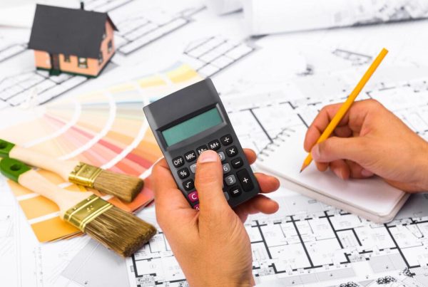 A calculator, construction drawings, paint samples, and brushes on a table symbolize smart renovation planning and a carefully managed budget for a home renovation.
