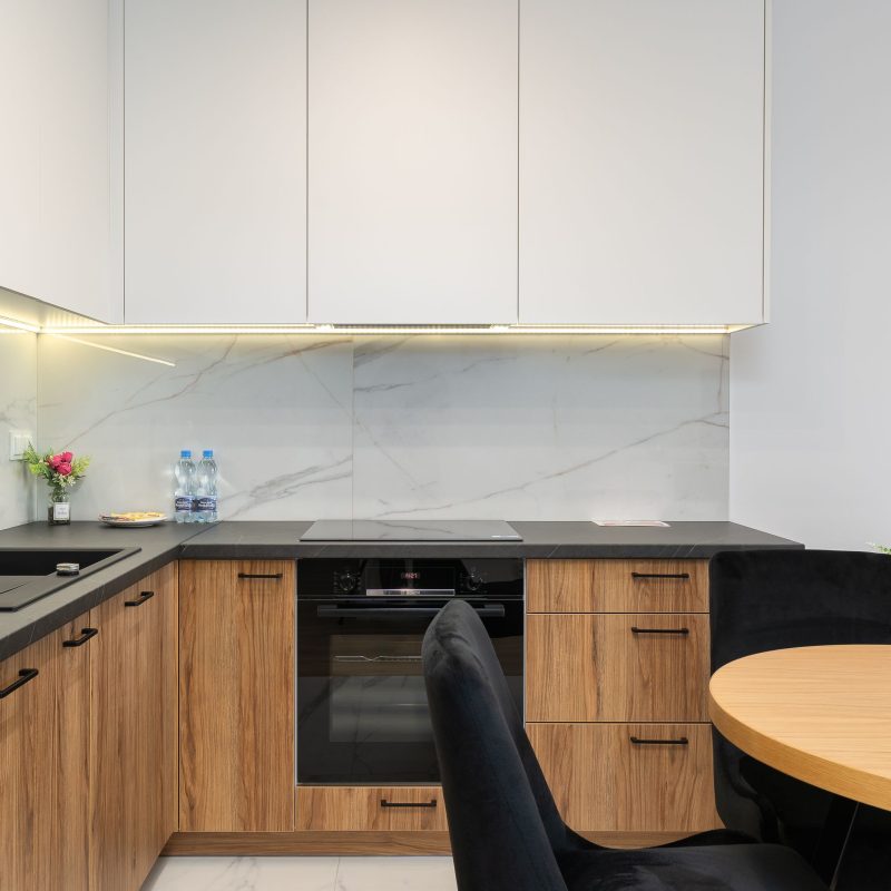 Modern, functional kitchen with wooden cabinet fronts, a dark countertop, white upper cabinets, and stylish LED lighting. The practical layout ensures comfort and efficient cooking.