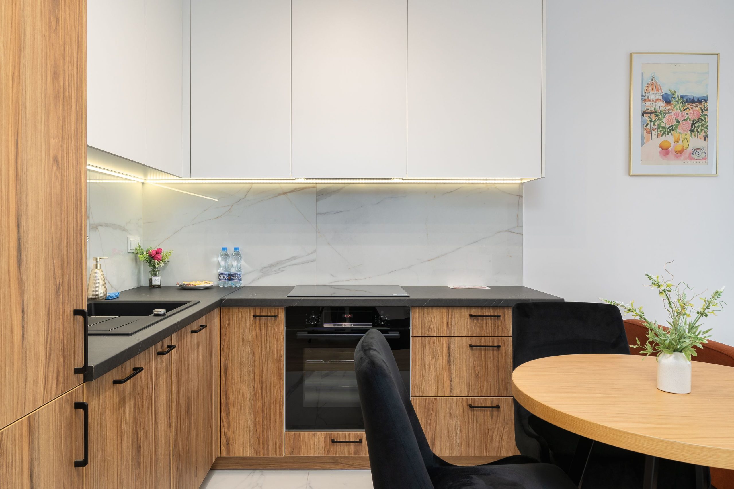 Modern, functional kitchen with wooden cabinet fronts, a dark countertop, white upper cabinets, and stylish LED lighting. The practical layout ensures comfort and efficient cooking.
