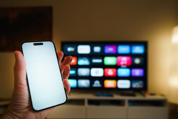 shows a person holding a smartphone in front of a smart TV. The phone appears to be controlling the TV, illustrating a smart home setup that provides greater convenience and easy device management.