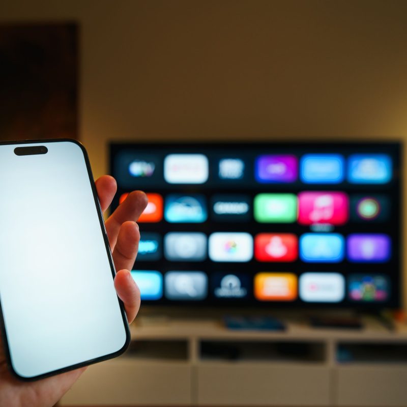 shows a person holding a smartphone in front of a smart TV. The phone appears to be controlling the TV, illustrating a smart home setup that provides greater convenience and easy device management.