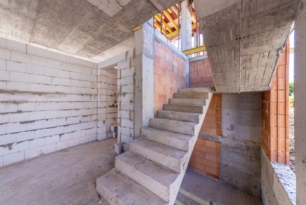 The structural framework of a house featuring a concrete staircase, unfinished walls, and a concrete ceiling.