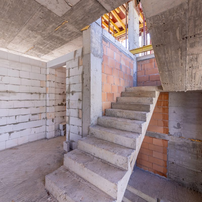 The structural framework of a house featuring a concrete staircase, unfinished walls, and a concrete ceiling.