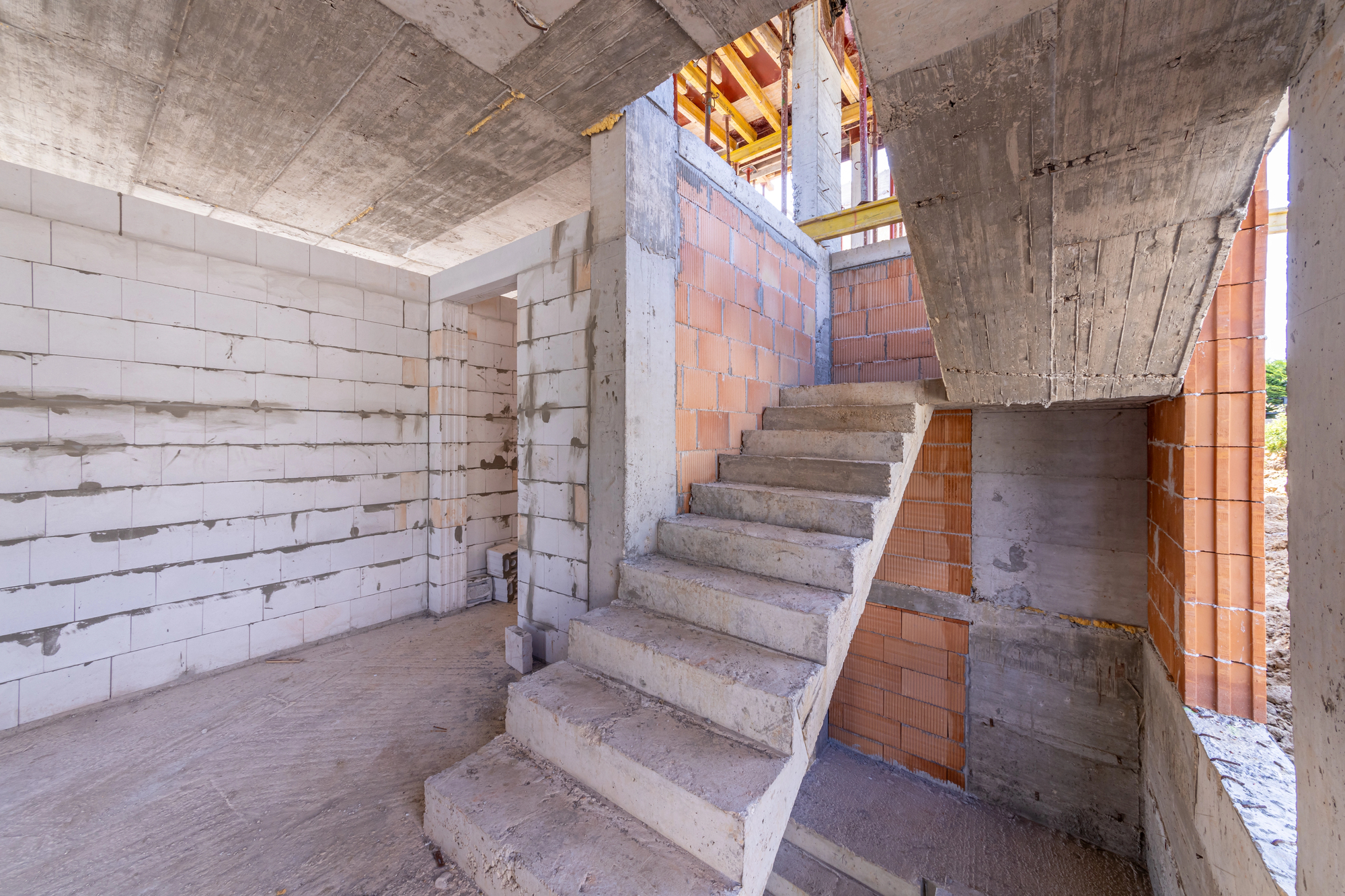 The structural framework of a house featuring a concrete staircase, unfinished walls, and a concrete ceiling.