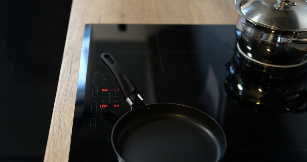 Modern black induction hob with pots and pans on active cooking zones – sleek, functional and stylish.