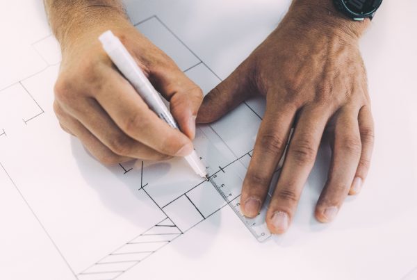 Op de foto zie je iemand die met een liniaal en een pen een technische tekening of bouwplan maakt.